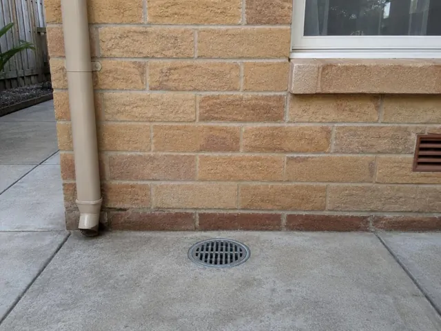Concrete courtyard gully grate beside brick wall and downpipe, paved area clean and dry in Maroubra